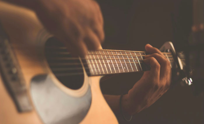 Hands playing an acoustic guitar in a dimly lit room, focusing on rich details of the strings and fingers.