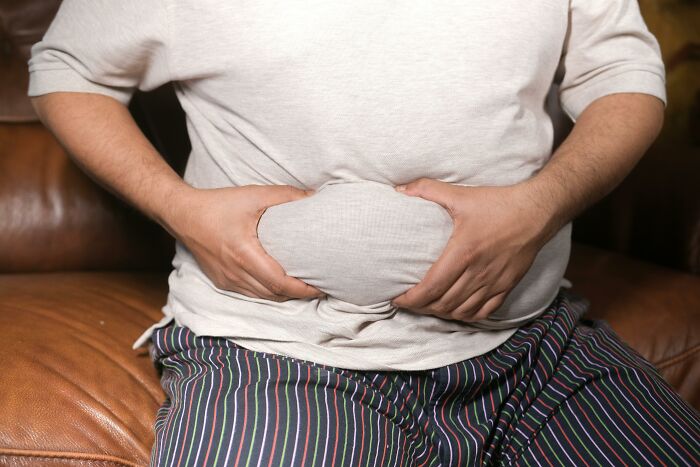 Person holding stomach, illustrating genetic blessings and weaknesses, wearing a white shirt and striped pants.