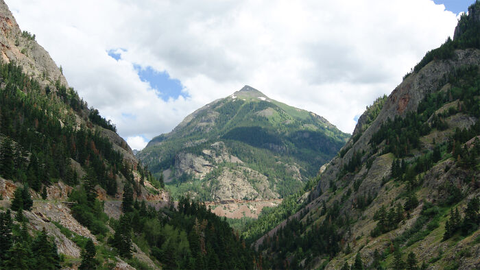 Scenic view of a mountainous pass, part of legendary American road routes surrounded by lush greenery under a cloudy sky.