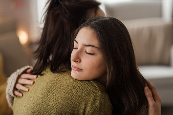 Teen girl hugging mother, eyes closed, highlighting babysitter volunteering tension. Teen girl hugging mother, eyes closed, highlighting babysitter volunteering tension.