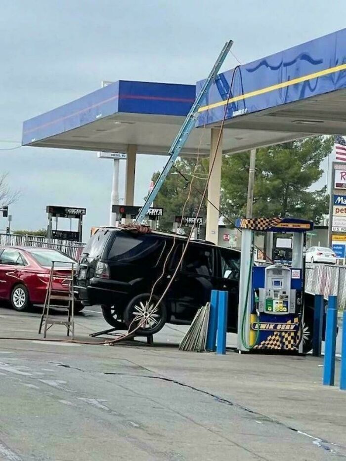 Improvised car repair at gas station with ladder and ropes supporting vehicle lift by redneck engineers.