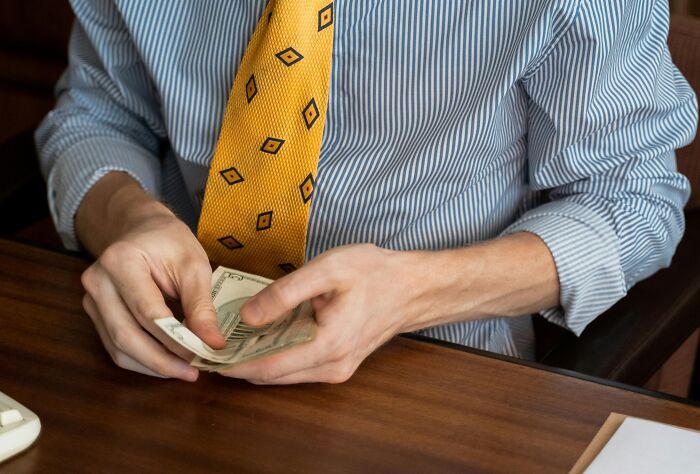Person in striped shirt and yellow tie counting money at office desk, relating to jokes about office themes.