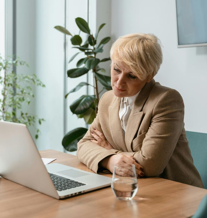 Person in a beige blazer looking at a laptop in an office setting.