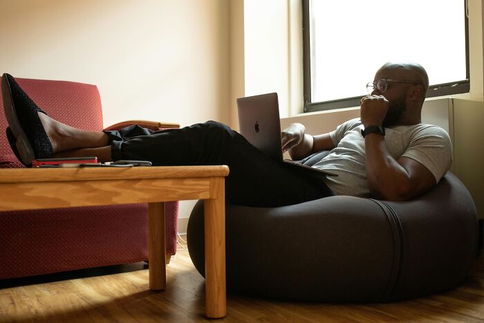 Man relaxed on a bean bag, working on a laptop, embodying jokes-about-office vibes in a casual setting.