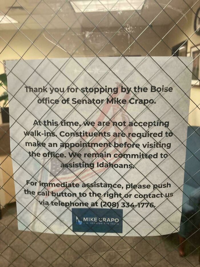 Sign on a wire-reinforced glass door indicating no walk-ins allowed at a government office, reflecting modern life boring dystopia.