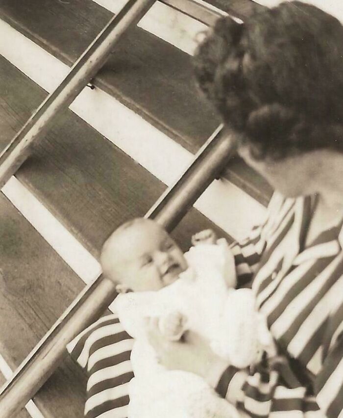 A woman in striped clothing holds a baby on a wooden staircase, showcasing a fascinating historical moment.