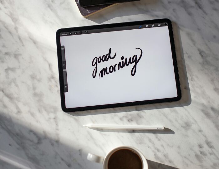 Tablet displaying "good morning" on marble surface beside a cup of coffee. Social rules people ignore in morning routines.