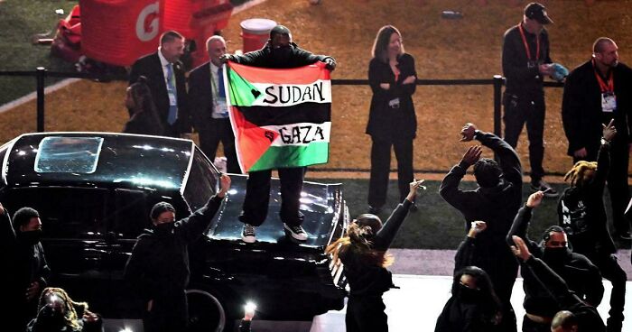 Person holding Sudan Gaza flag during chaotic good morally grey acts at a public event with a crowd and security present.
