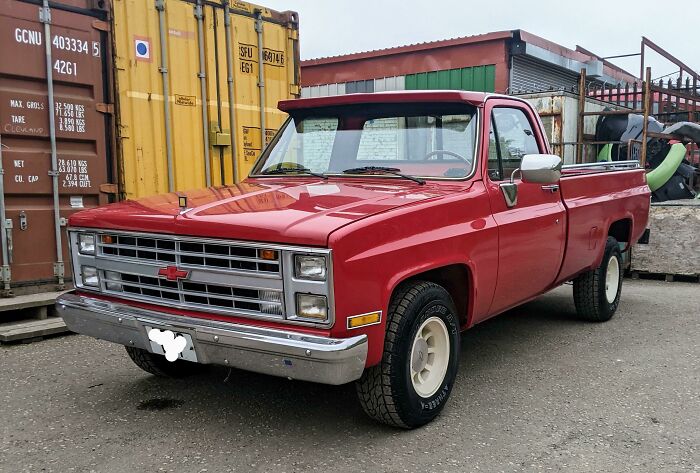 Red vintage truck parked by shipping containers, showcasing classic car design.
