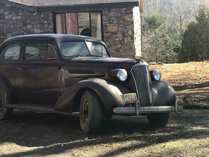 Vintage car parked in front of a rustic stone house under sunlight.
