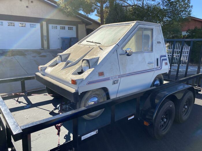 Vintage car on a trailer, showcasing unique design features, parked in a residential neighborhood.