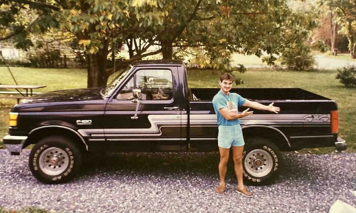 Man showcasing a vintage truck in a backyard setting, with vibrant greenery and a picnic table in the background.