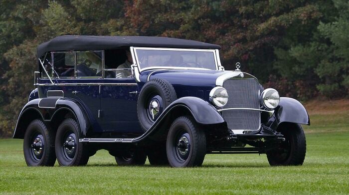 A classic vintage car with a dark blue body and black roof parked on grass.