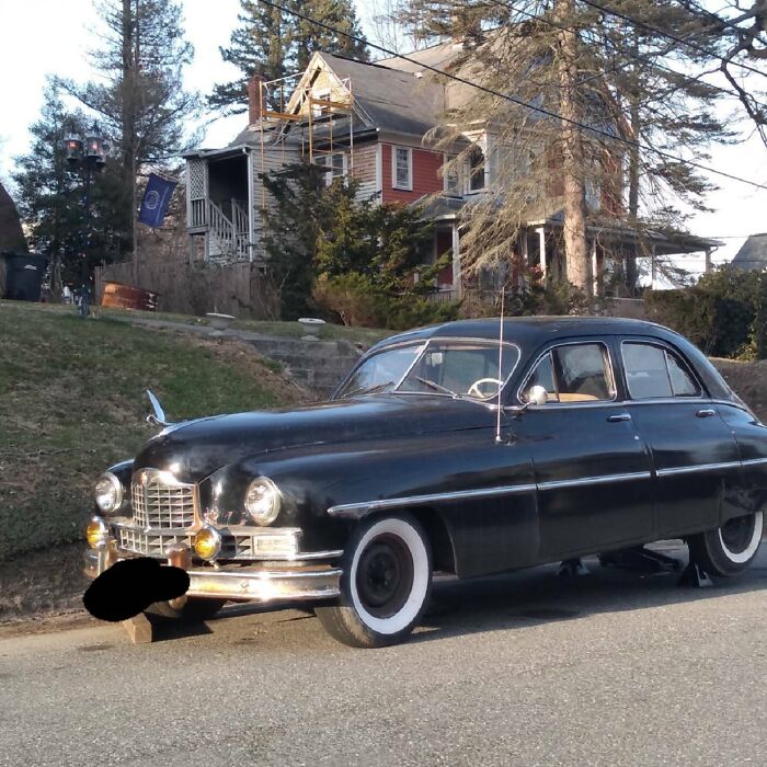 A black vintage car parked on a street in front of a house, showcasing classic design.