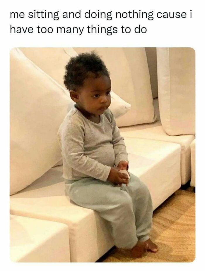Toddler sitting on a couch looking bored with caption about doing nothing despite having many tasks, humor coping mechanism post.