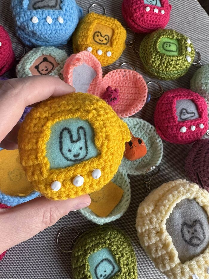 Hand holding a colorful DIY crocheted toy with animal faces, surrounded by similar handmade projects.