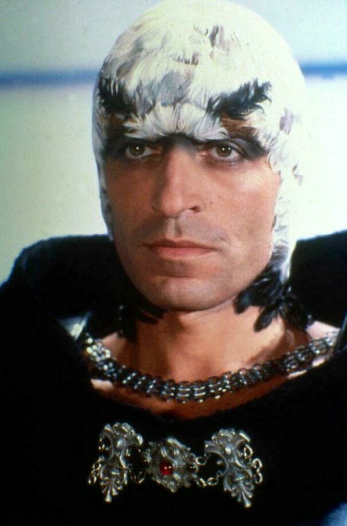 Man in a feathered costume with a serious expression from a classic film, evoking nostalgia.