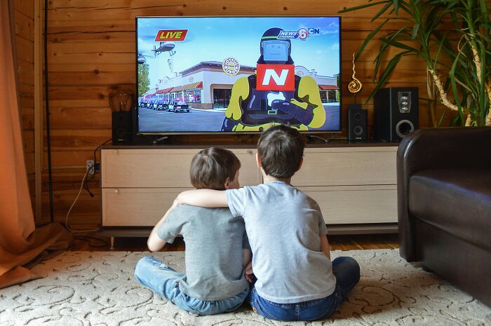 Two boys sitting on the floor, watching a news report on TV, embracing a brilliant life hack moment in their living room.
