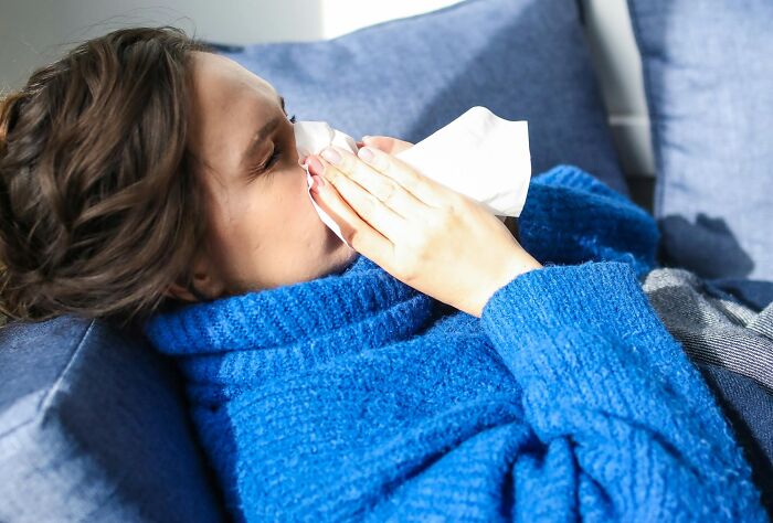 Woman in a blue sweater using brilliant life hacks to alleviate symptoms with a tissue.