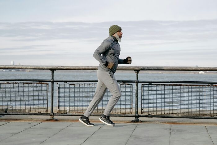 Man jogging by the waterfront, wearing a beanie and tracksuit, embodying brilliant life hacks for fitness.