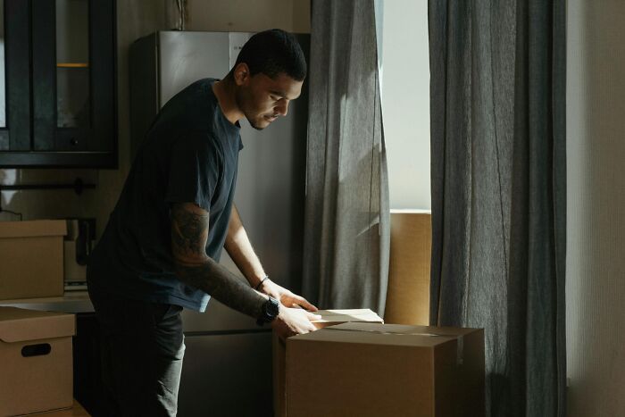 Man packing a box in a dimly lit room, illustrating brilliant life hacks for organizing and moving efficiently.