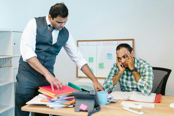 Two colleagues experiencing work-struggles with paperwork at a cluttered office desk.