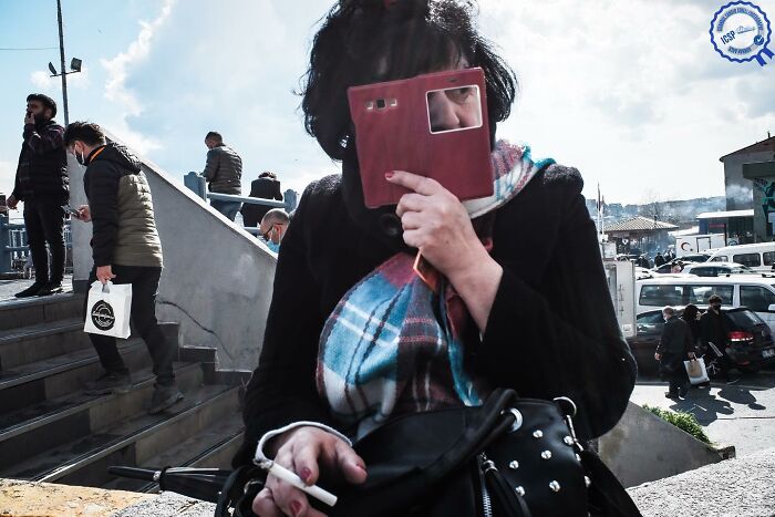 Person holding a phone case to their face on a busy street, capturing a unique moment.