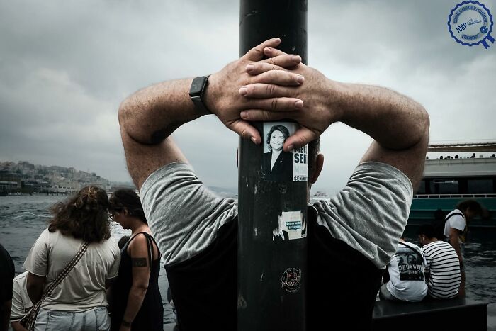 Person leaning against a pole near waterfront, capturing a unique street perspective.