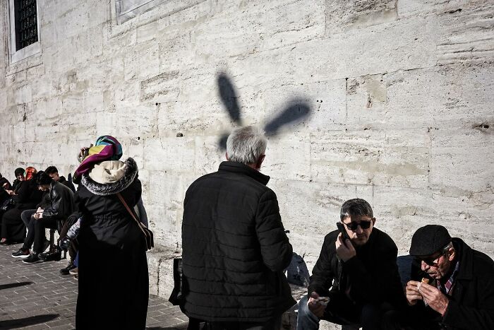 A man stands by a wall casting a shadow with rabbit ears, exemplifying Gökhan Arer's unique street perspective.