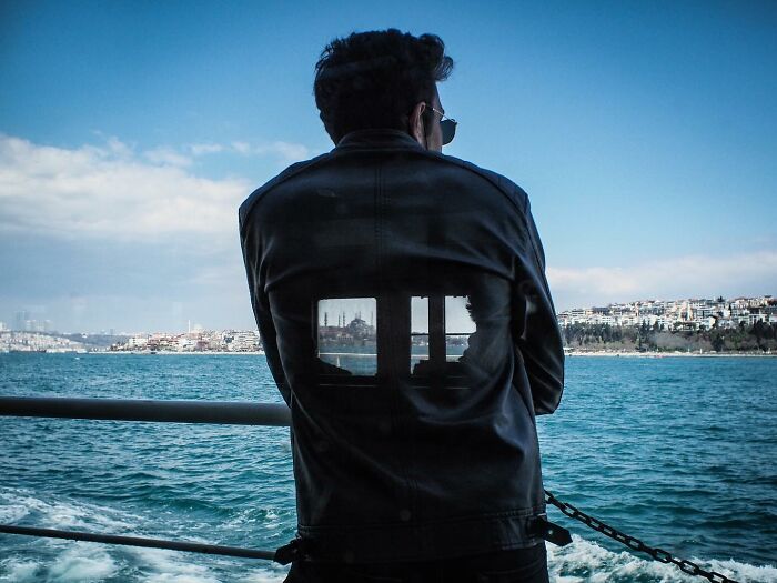 Person on a boat wearing a jacket, with cityscape reflection visible, exemplifying Gökhan Arer's unique street perspective.
