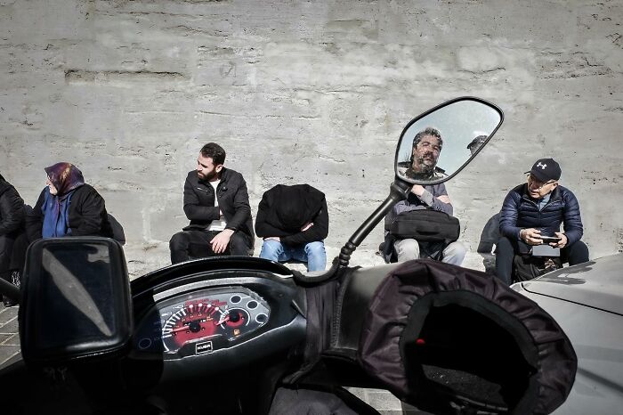 People sitting on a wall observed from a motorcycle's mirror, showcasing Gökhan Arer's unique street perspective.