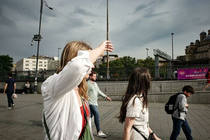 Two women walking in the street, one shielding her eyes from the sun, showcasing Gökhan Arer's unique urban perspective.