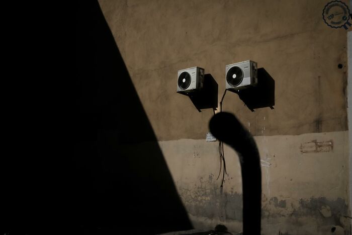 Two air conditioning units on a wall cast unique shadows, showcasing Gökhan Arer's distinct perspective of the streets.