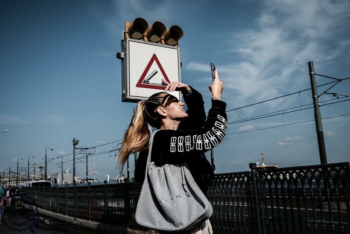 A woman on the street takes a photo with a smartphone, capturing a unique perspective under a traffic sign.