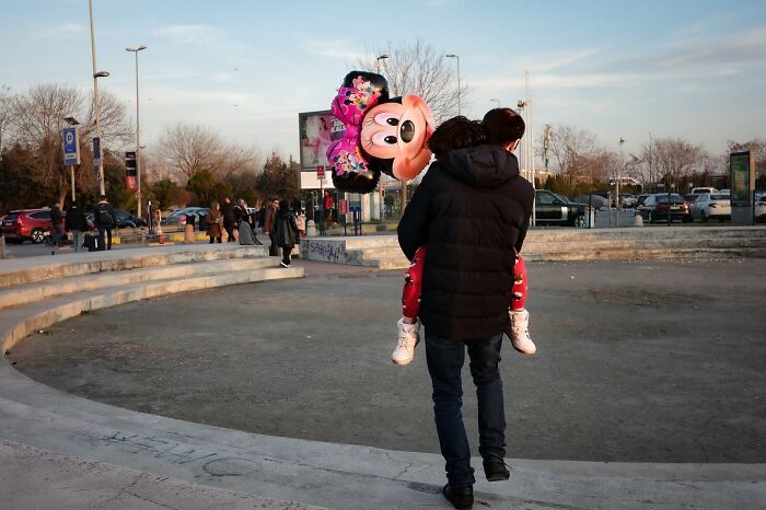 Man carrying child with Minnie Mouse balloon in an urban setting, capturing Gökhan Arer's unique street perspective.