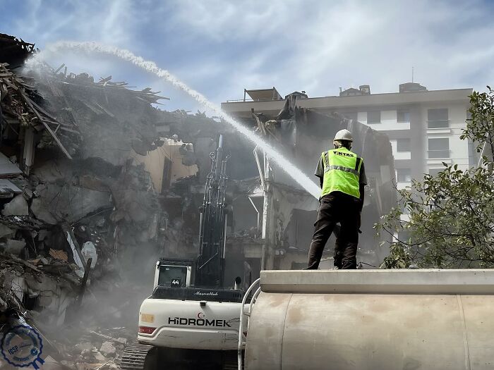 Construction worker controlling rubble with water, highlighting Gökhan Arer's unique perspective on urban streets.