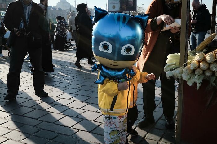 Child with cartoon balloon on bustling street, capturing Gökhan Arer's unique street view.