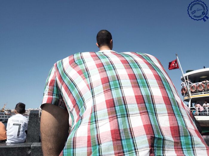 Man in plaid shirt creating optical illusion, making him appear large, showcasing Gökhan Arer's unique street perspective.