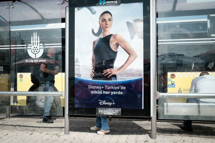 A perfectly timed street photo showing a person's legs aligning with a poster, creating an illusion at a bus stop.