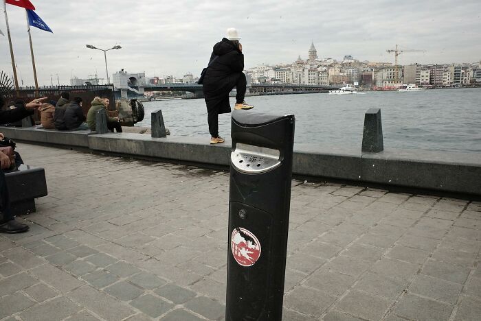 Streets seen differently: a person in white hat overlooking the water, standing on a ledge near a riverside path.