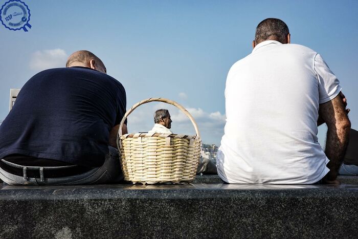 Two men sitting on a ledge with a basket between them, demonstrating Gökhan Arer's unique street photography perspective.