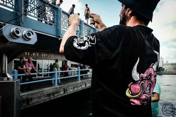 Man in a black shirt photographing people on a bridge; a creative street photography moment by Gökhan Arer.