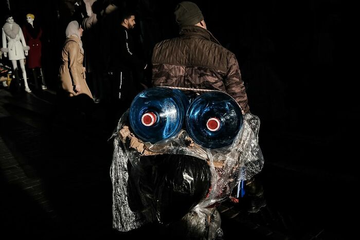 Man on the street with two large water bottles, creating a unique eye-like visual, showcasing Gökhan Arer's perspective.