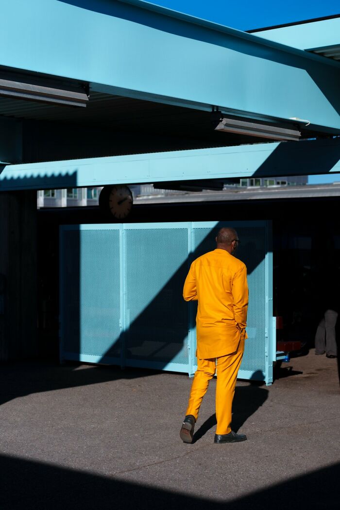 Person in vibrant orange suit walking under blue structure, capturing the essence of Oslo’s streets.