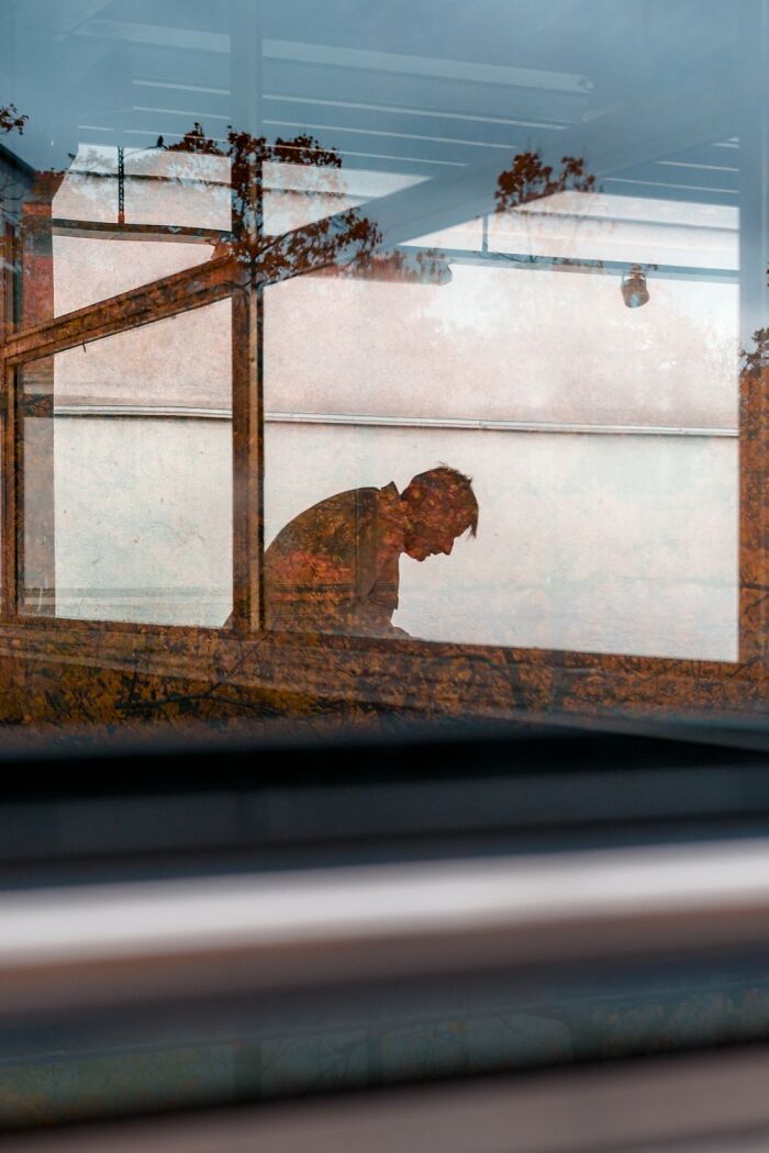 Silhouette of a person through a window, capturing the essence of Oslo's streets with reflected autumn leaves.