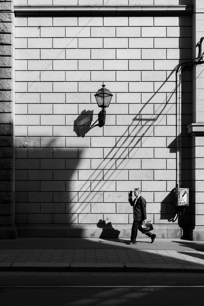 Man walking by a shadowed wall in Oslo, carrying a briefcase, embodying the essence of street photography.