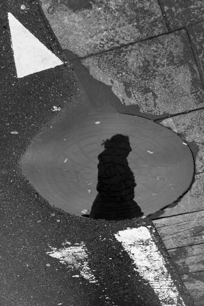 Shadow of a person in a puddle reflecting Oslo and Stockholm's streets essence, captured in black and white.