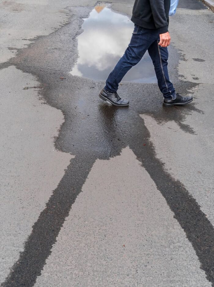 Man walking past a puddle reflecting clouds on Oslo street; captures the essence of urban life.