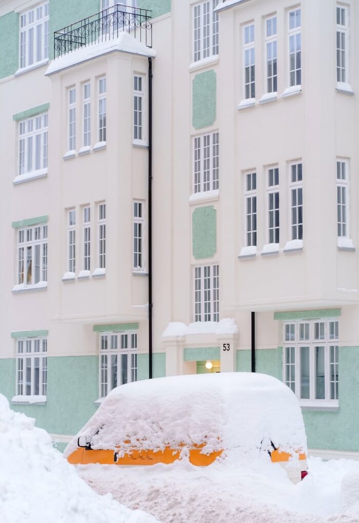 Snow-covered car in front of pastel-colored building, capturing Oslo and Stockholm's street essence.