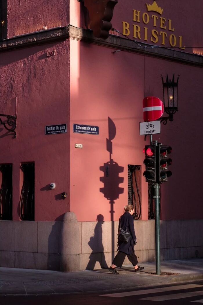 Street photography capturing a person walking past Hotel Bristol in Oslo, with shadows cast on the wall.